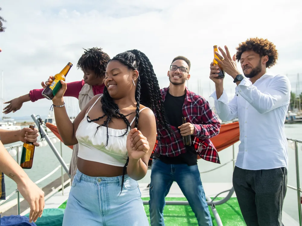 Friends dancing and raising bottles together on a boat deck in daylight